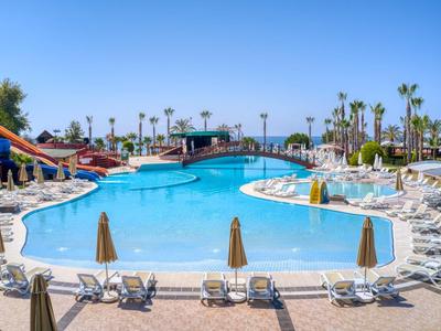 Sunny outdoor pool with slides, palm trees, and lounge chairs at a resort.