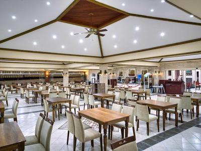 Spacious hotel dining area with wooden tables, cushioned chairs, and bright ceiling lights.
