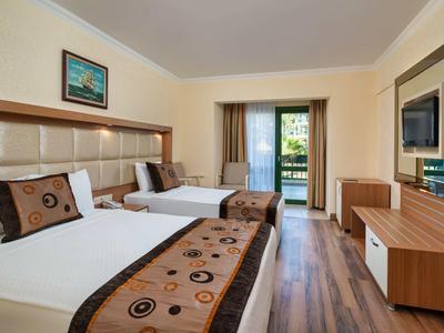 Hotelzimmer mit zwei Betten, Holzfußboden und Balkon mit Blick ins Grüne.