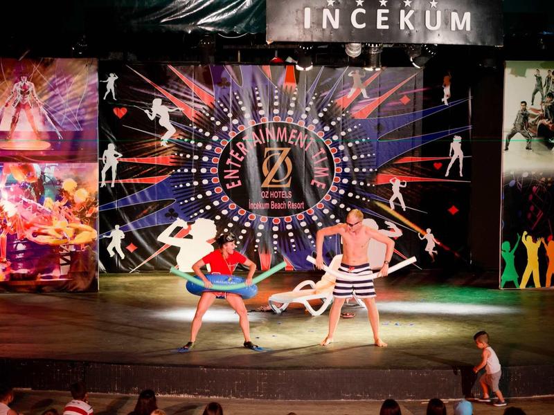 Two performers in colorful costumes dancing on a lit stage with vibrant background art.