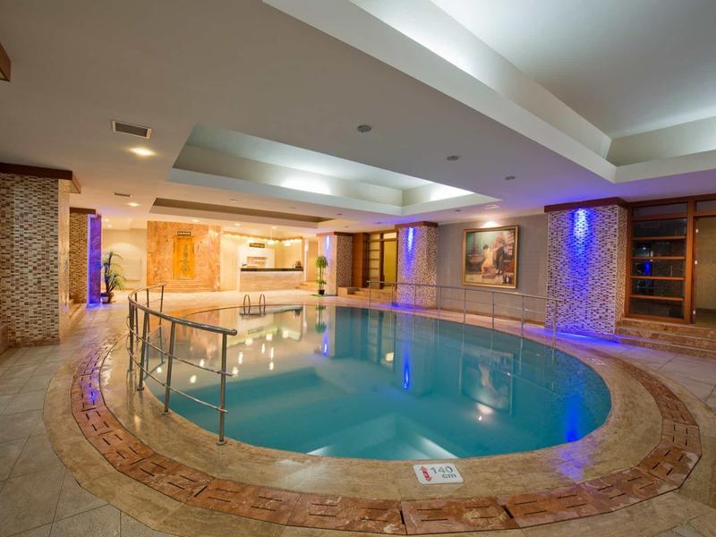 Indoor oval pool with stone tiles and blue ambient lighting in a hotel wellness area.