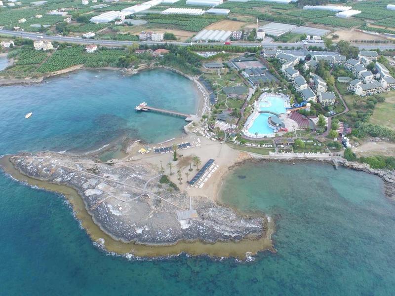 Coastal resort with pools, green areas, pier, and surrounding blue sea, viewed from above.