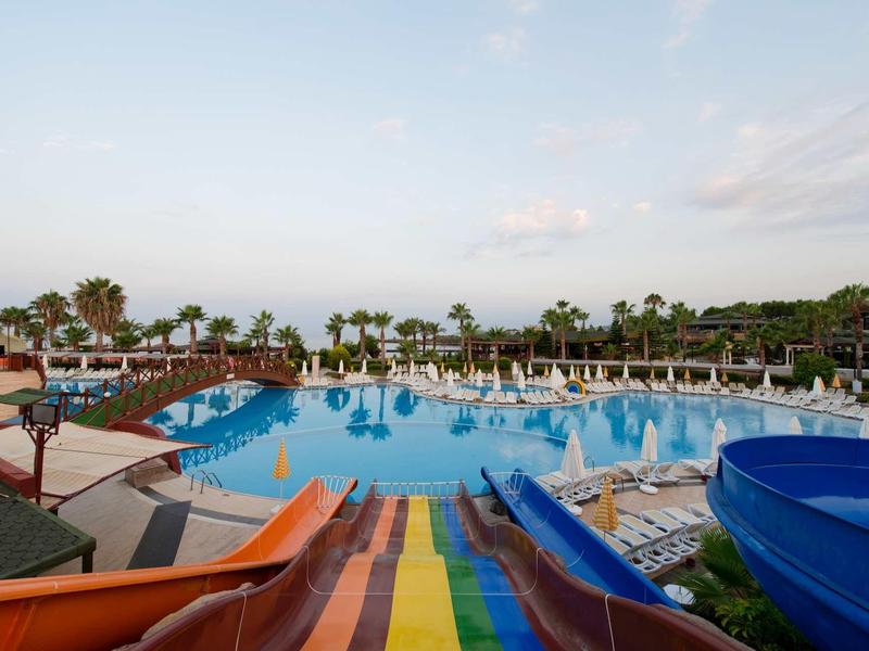 Wide pool with colorful water slides and palm trees at a resort under a clear sky.