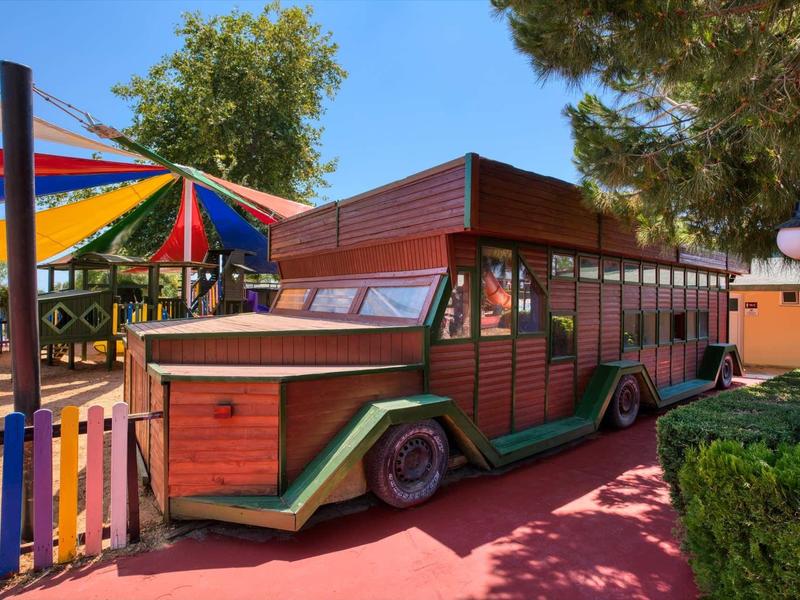 Colorful wooden miniature train ride next to umbrellas and trees in a play area.