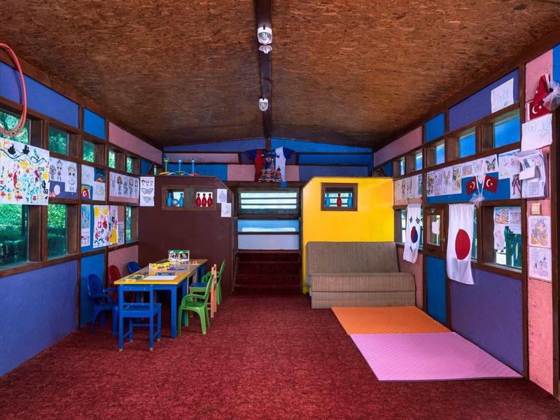 Colorful children's playroom with small tables, chairs, and art on walls under a wooden ceiling.