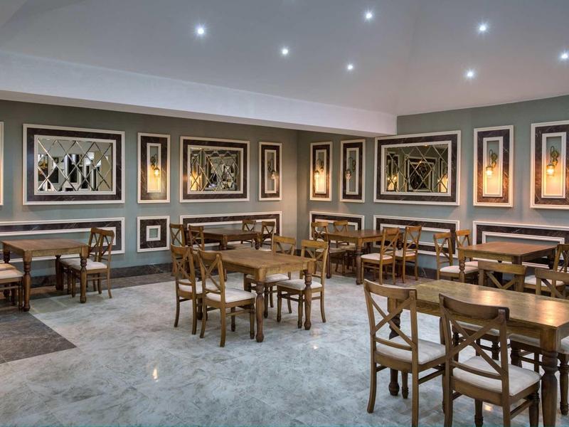 Spacious hotel dining area with wooden tables and chairs, framed artwork, and recessed lighting.