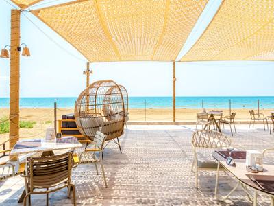 Open beach view from a covered terrace with modern seating and a wicker chair.