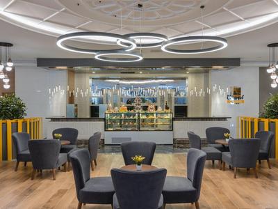 Modern hotel lobby area with round tables, armchairs, and stylish ceiling lights.