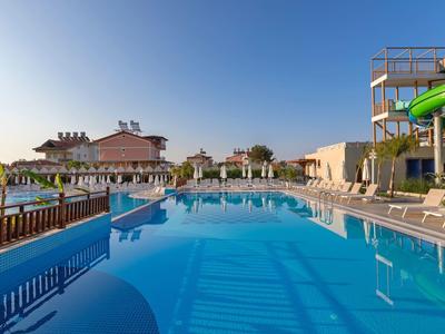 Grande piscina dell'hotel con acqua limpida, lettini e scivoli d'acqua sotto un cielo sereno.
