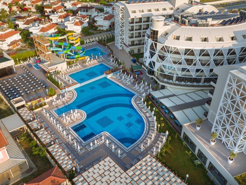 Grande resort alberghiero con piscine multiple, scivoli d'acqua e lettini vicino alla costa.
