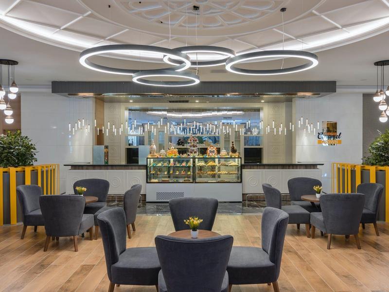 Area bar di hotel arredata modernamente con tavoli rotondi, poltrone e luci da soffitto eleganti.