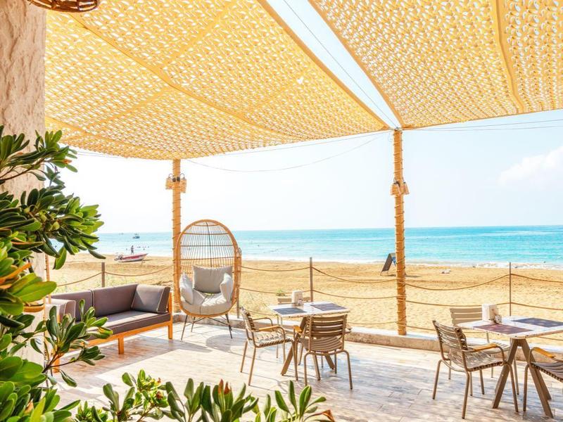Ristorante sulla spiaggia con tende parasole, tavoli e vista mare in una giornata di sole.