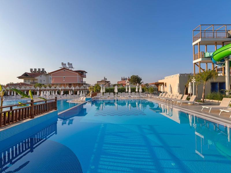 Grande piscina dell'hotel con acqua limpida, lettini e scivoli d'acqua sotto un cielo sereno.