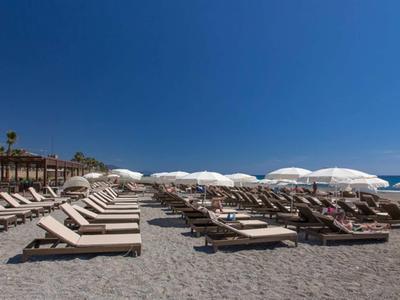 Strand mit vielen weißen Liegestühlen und weißen Sonnenschirmen unter klarem blauem Himmel.