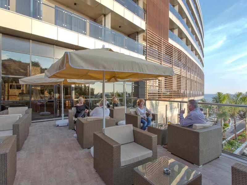 Espace extérieur d'hôtel moderne avec mobilier lounge et parasol sur terrasse par temps ensoleillé.