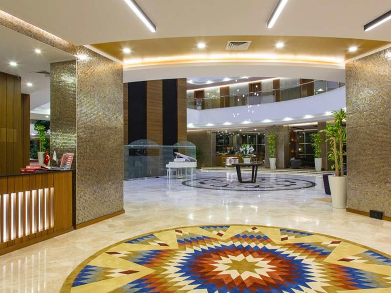 Hall d'hôtel lumineux avec tapis rond coloré et réception moderne sous reflet au plafond.