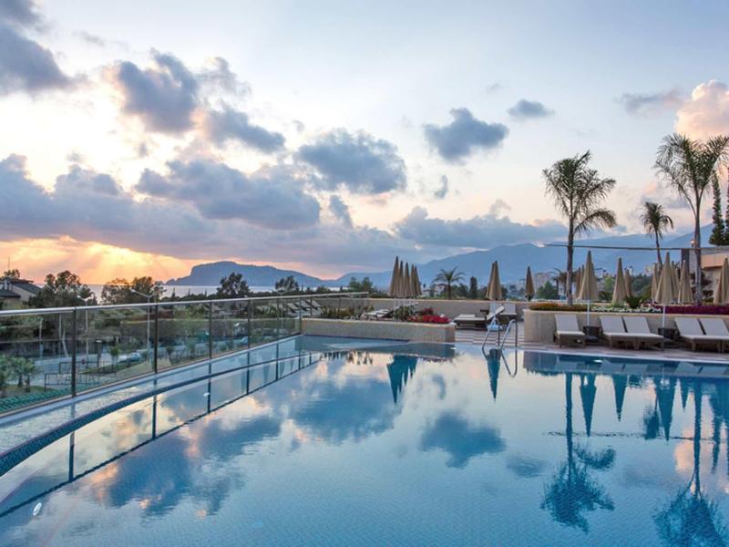 Piscine à débordement avec transats et palmiers devant un paysage montagneux au coucher du soleil