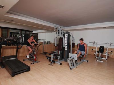 Gimnasio moderno con suelo de madera, varias máquinas de ejercicio y dos personas entrenando.