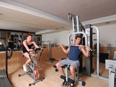 Dos hombres entrenan en un gimnasio luminoso de hotel con varios equipos de ejercicio.