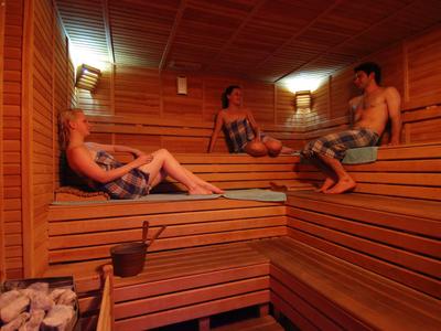 Three people relax in a wooden sauna with warm lighting.