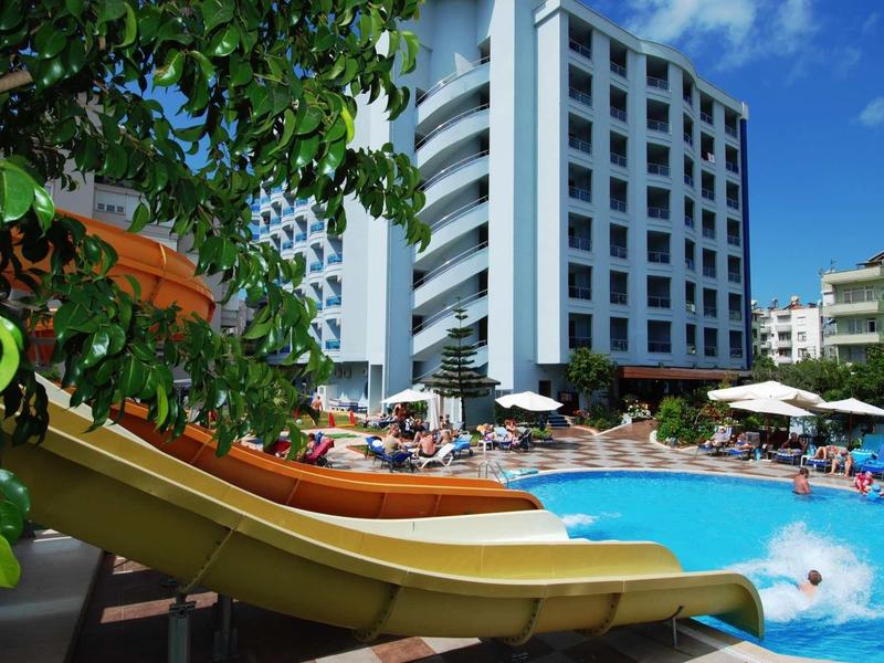Modern hotel with outdoor pool and water slide under blue sky.