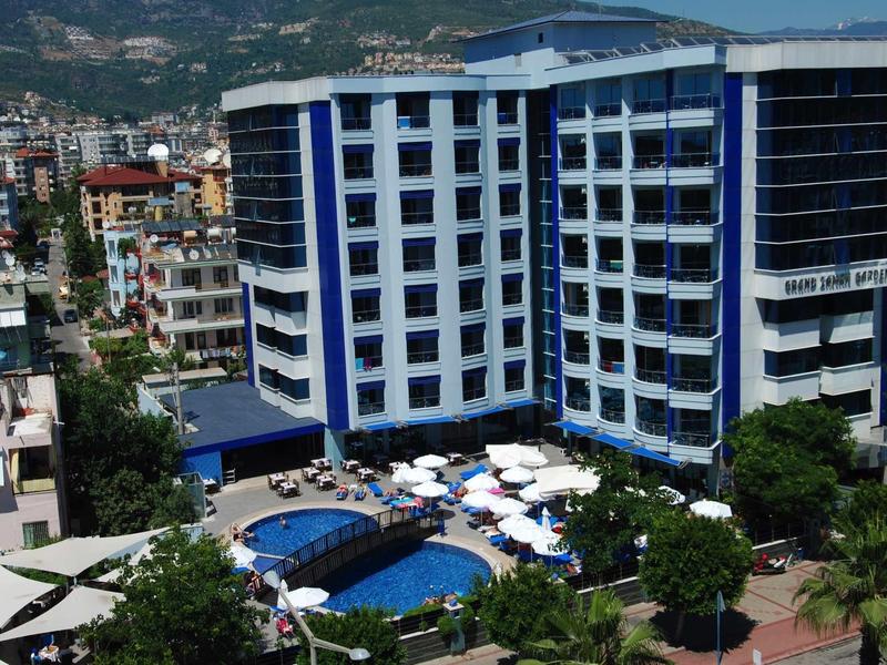 Modern hotel complex with pool and umbrellas in a city with mountains in the background.