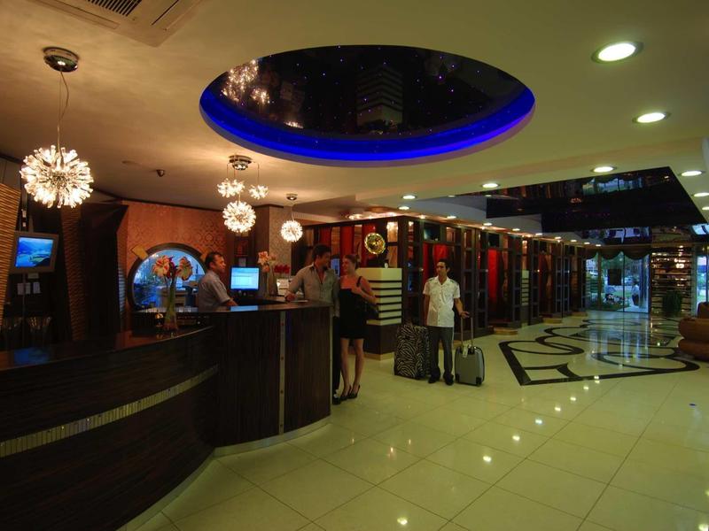 Hotel lobby with reception, modern lighting, and guests with luggage.