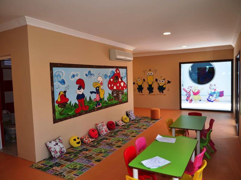 Colorful children's playroom with small tables, chairs, and cartoon-themed wall decorations.