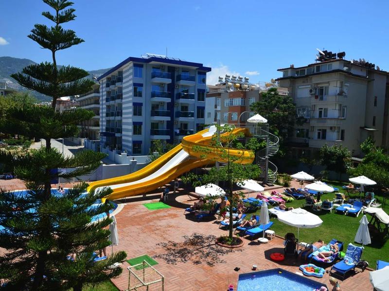 Hotel pool with large water slides, sun loungers, and umbrellas under a blue sky