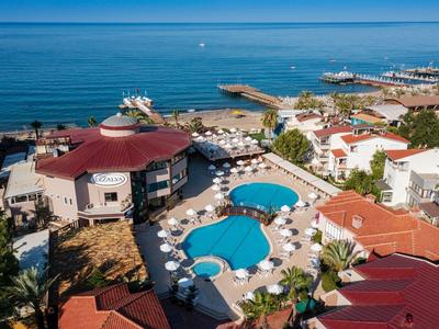 Poolanlage mit blauen Pools, Sonnenschirmen und roten Dächern an der Küste mit Blick auf das Meer.