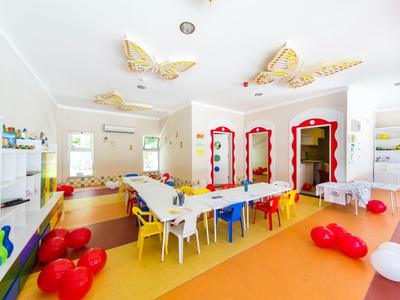 Heller, bunter Raum mit Tischen, Stühlen, roten und weißen Luftballons und großen Schmetterlingsdekorationen.