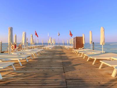 Een houten pier met witte ligbedden en parasols leidt naar de rustige zee onder een heldere hemel.
