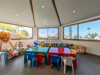 Kleurrijke speelkamer voor kinderen met kleine tafels en stoelen, omgeven door grote ramen.