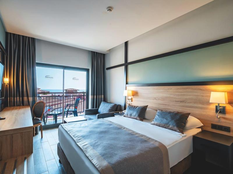 Modern hotel room with large bed, wooden furniture, and balcony overlooking outdoors.