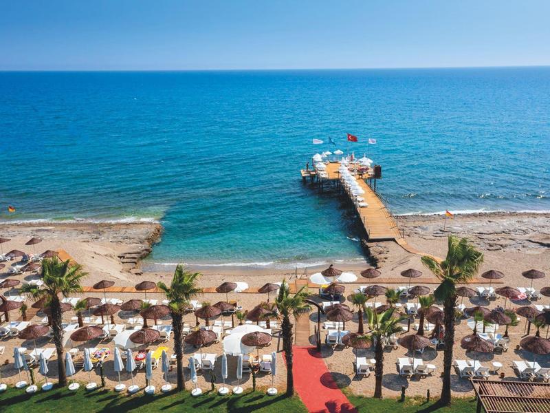 Beach resort with sun loungers, umbrellas, palm trees, and a pier extending into the sea.