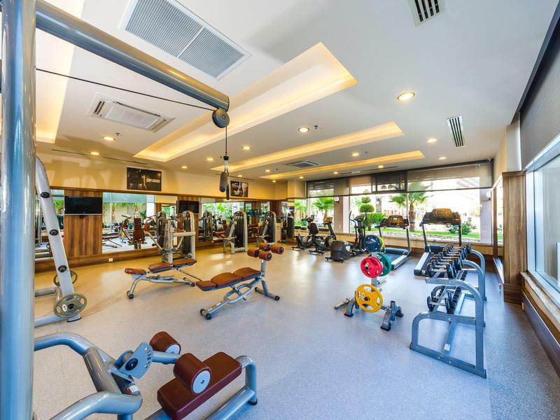 Spacious gym with modern equipment, large windows, and bright lighting in a hotel setting.