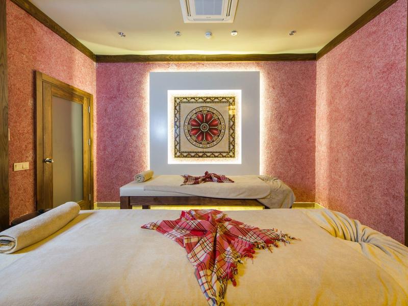 Cozy massage room with two beds, pink walls, and a decorative wall art with soft lighting.