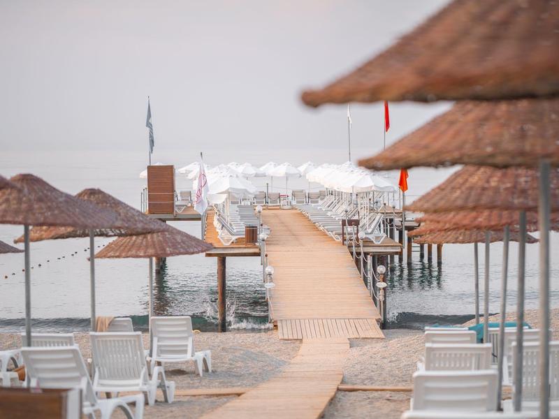 Wooden pier with thatched umbrellas and lounge chairs on a sandy beach by calm sea.