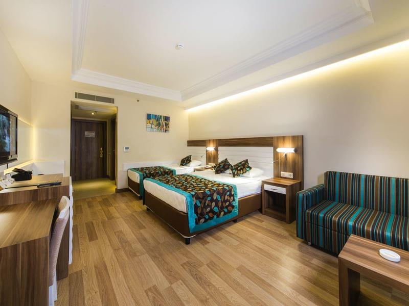 Modern hotel room with double bed, wooden floor, striped sofa, and warm lighting.