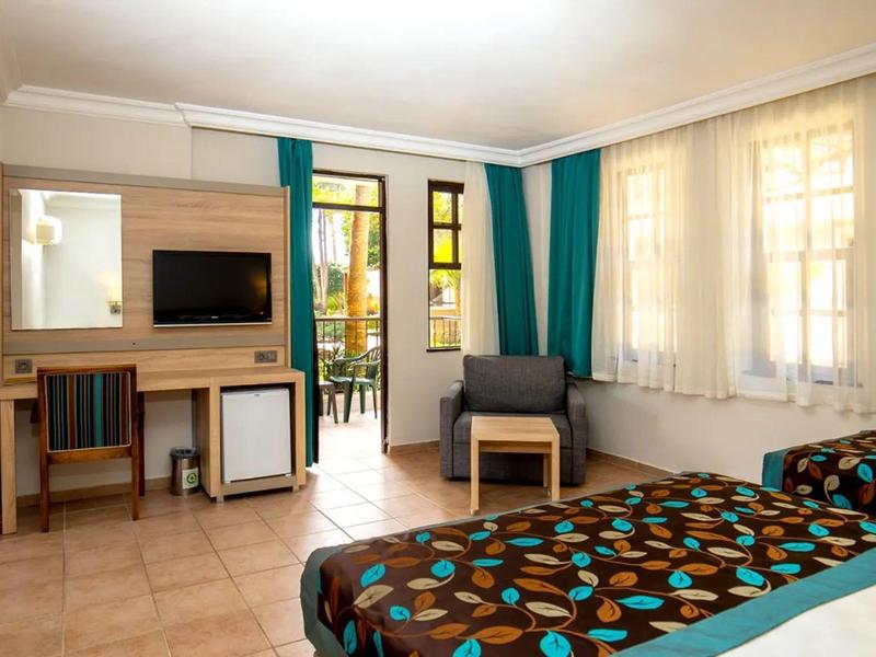 Bright hotel room with two beds, a desk, chair, TV, and large windows with curtains.