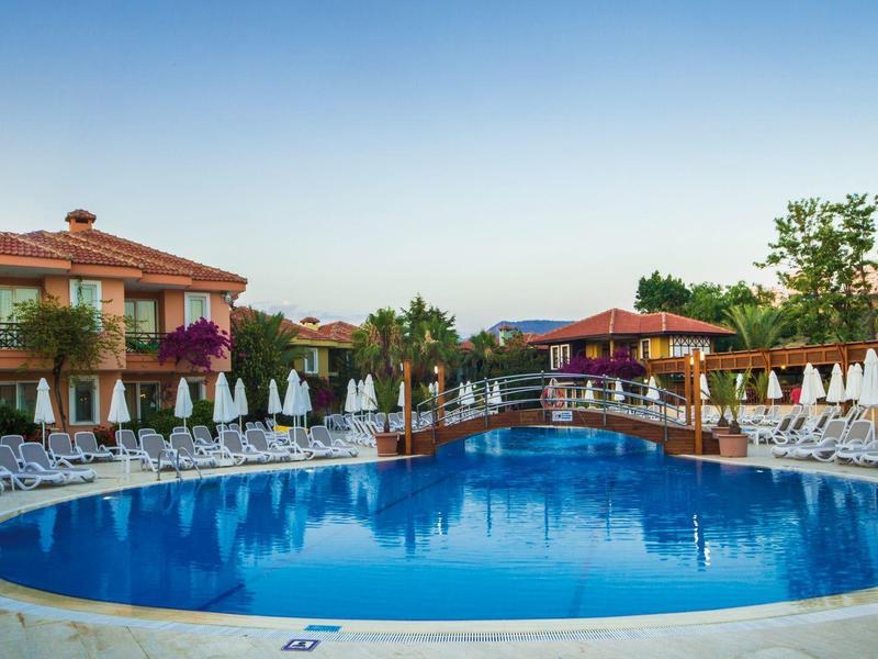 Outdoor hotel pool with lounge chairs and buildings under clear sky.