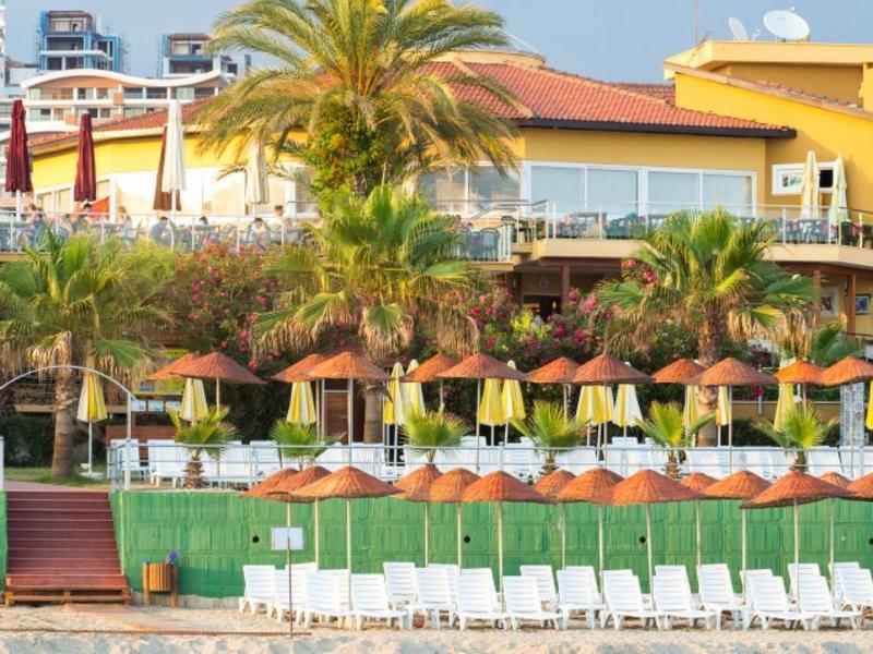 Beachfront resort with sun loungers, umbrellas, palm trees, and buildings in the background.