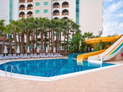 Schwimmbad mit bunten Wasserrutschen, Liegestühlen und Palmen vor einem Hotelgebäude.