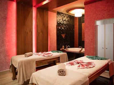 Ein ruhiger Wellnessraum mit zwei Massageliegen, roter Beleuchtung und weichen Handtüchern.