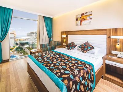 Helles Hotelzimmer mit Holzfußboden, großem Bett, buntem Bettüberwurf und Panoramafenster.