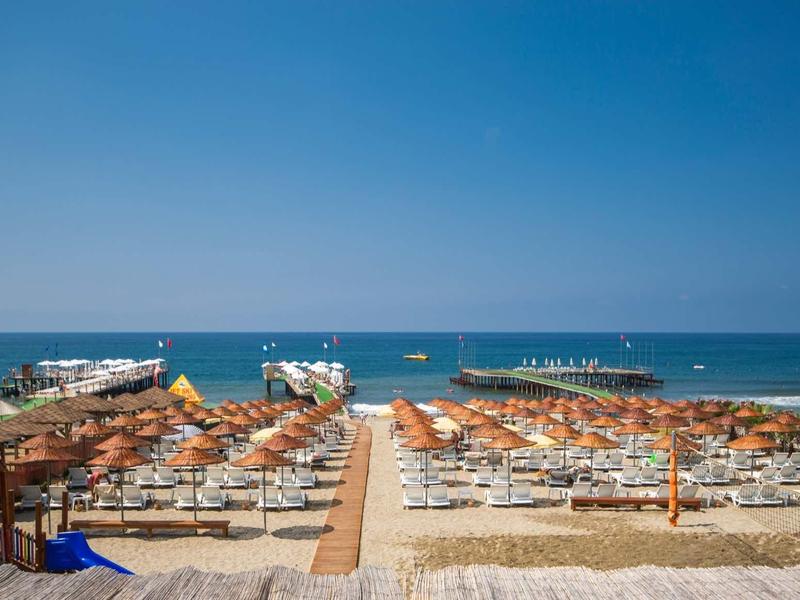 Pláž s oranžovými slunečníky a modrým mořem pod jasnou oblohou.