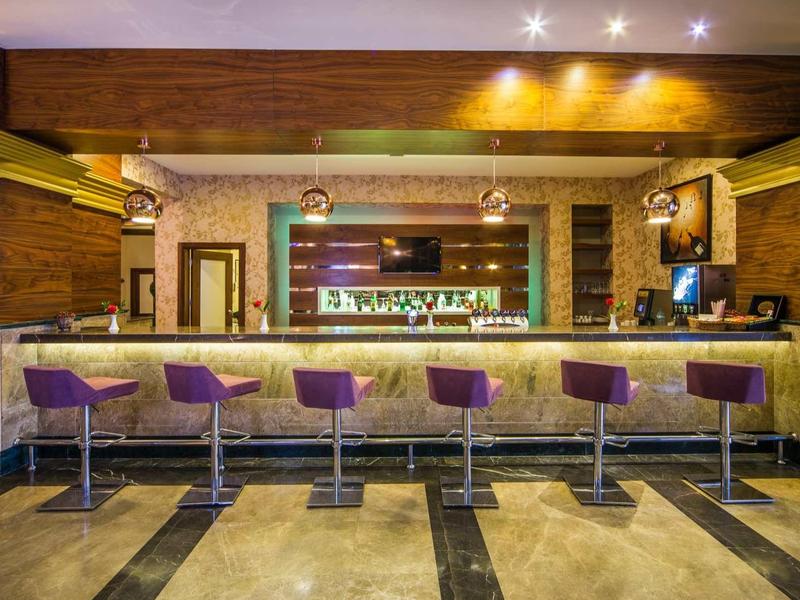 Moderní hotelový bar s fialovými stoličkami a teplým osvětlením.