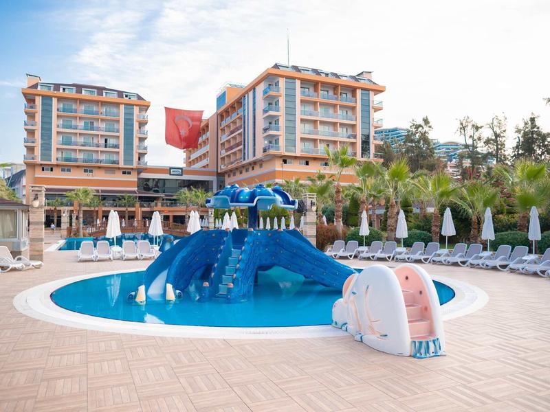 Dětský bazén s tobogány před moderním hotelem a lehátky.
