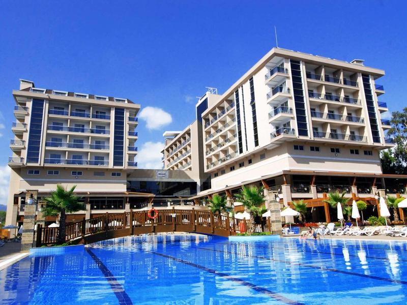 Moderní hotel s velkým modrým bazénem pod jasnou oblohou.