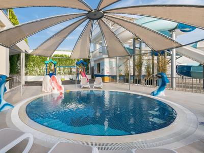 Okrągły basen kryty z zjeżdżalniami wodnymi i figurami delfinów pod przezroczystym dachem.